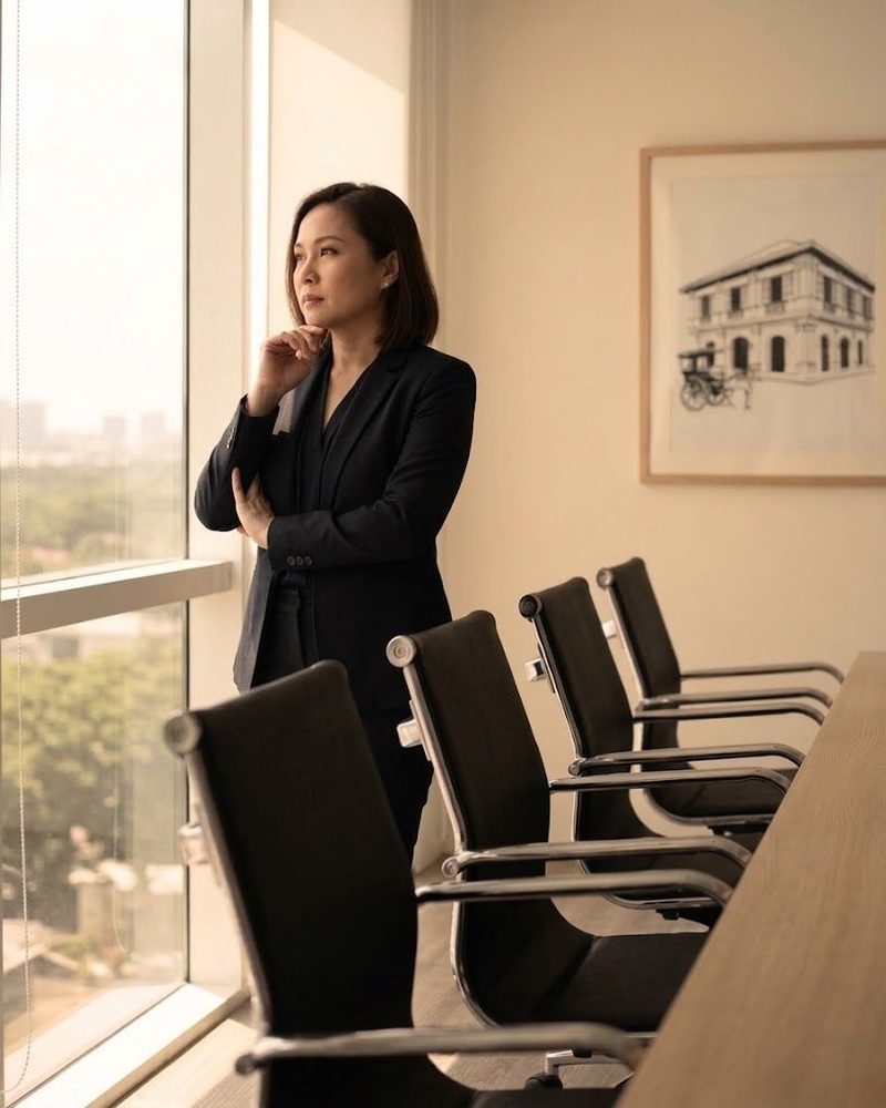 A woman standing at a boardroom window beside a row of empty chairs