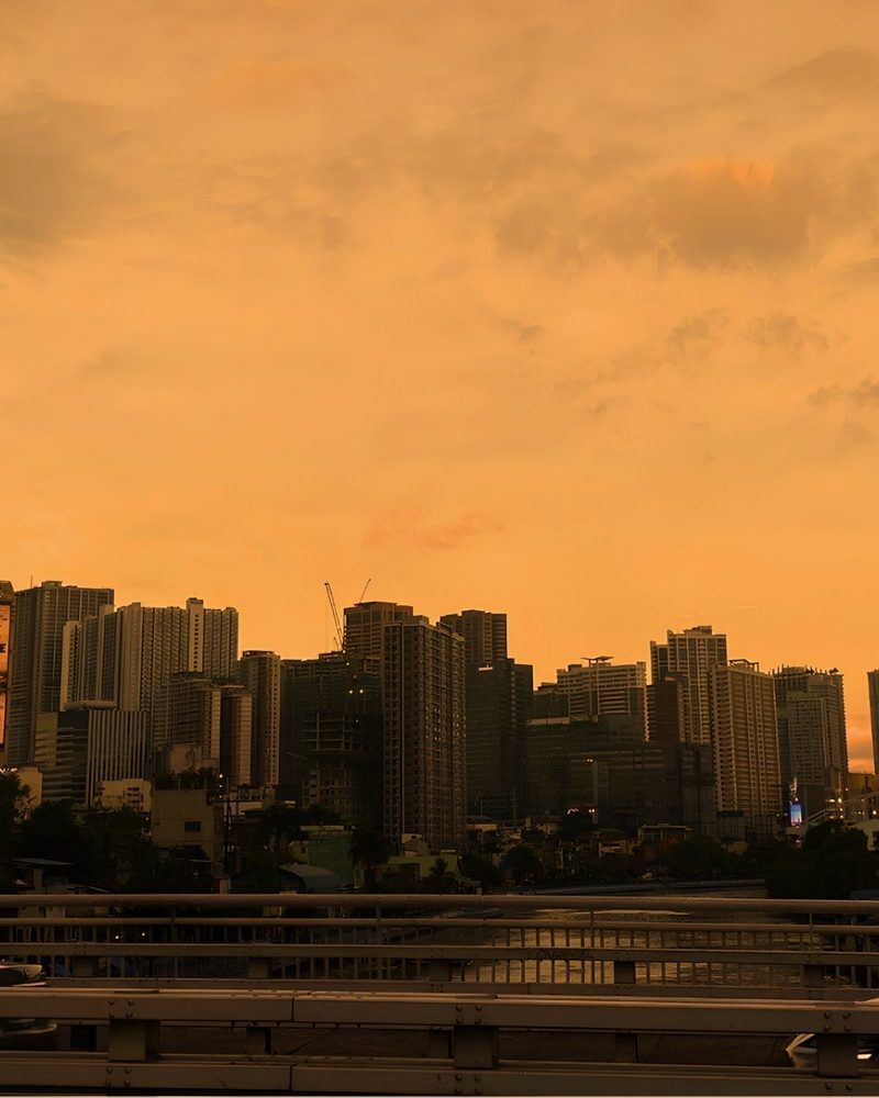 The Manila skyline under an orange sunset, seen from a bridge