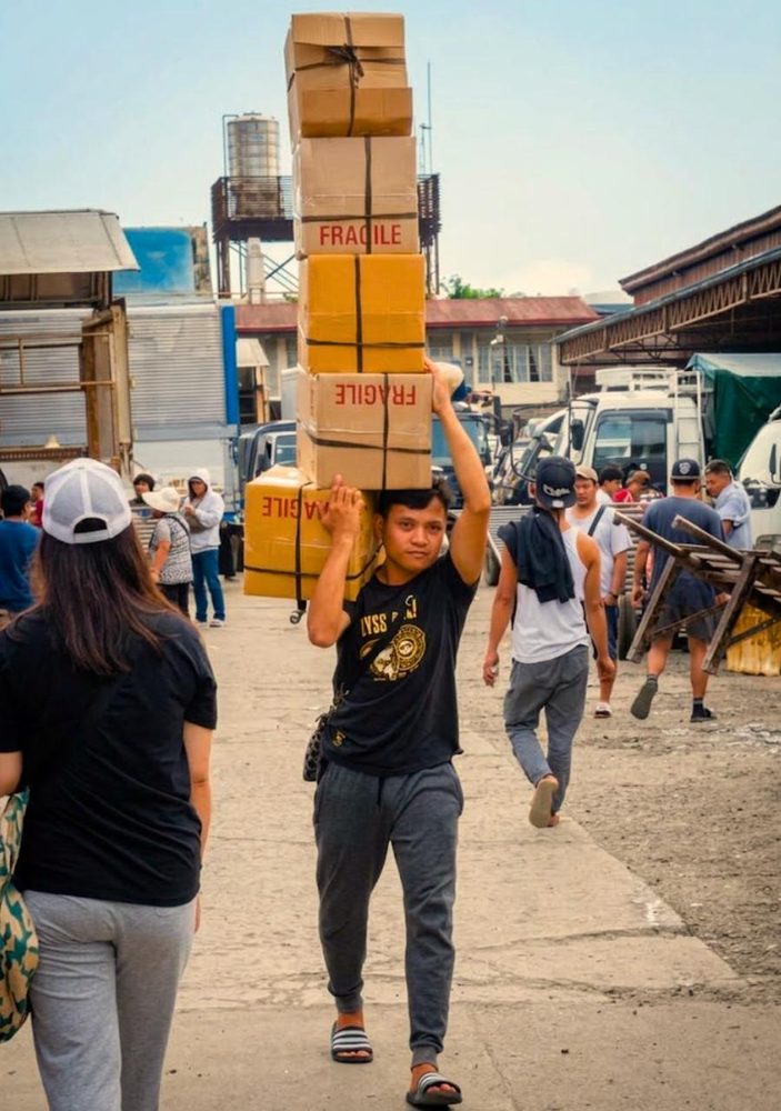 A man carrying a tall stack of boxes marked fragile through a busy street