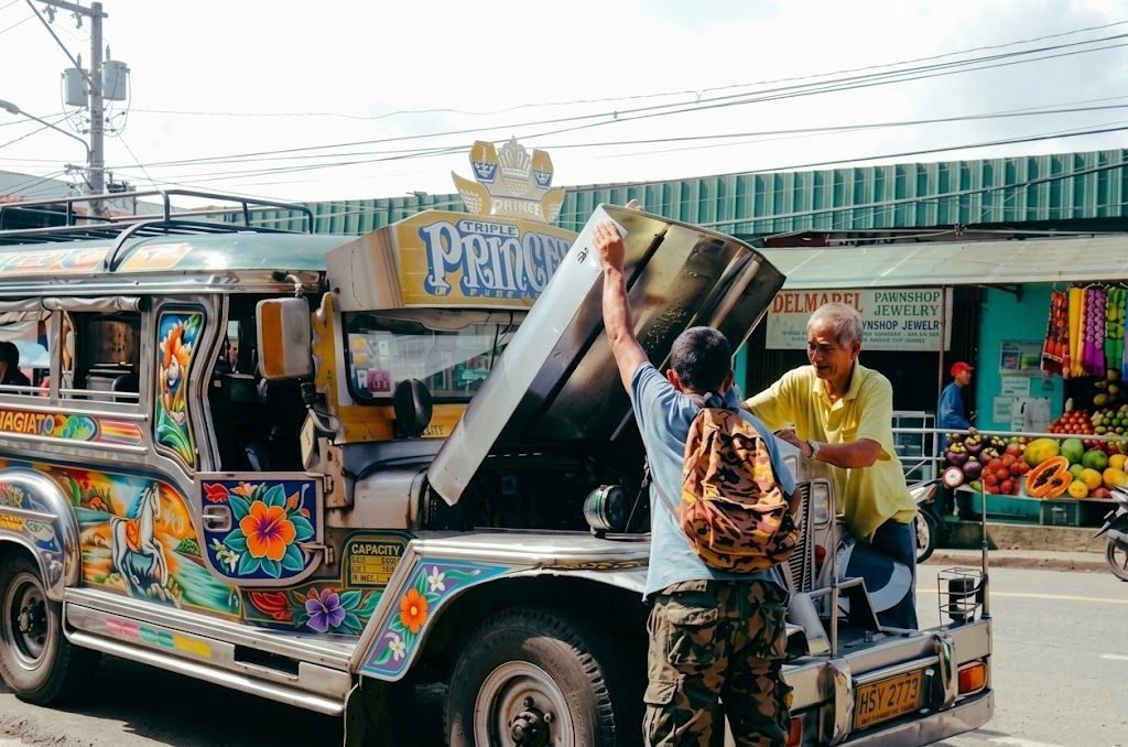 Two men working together to lift the hood of a jeepney on a Manila street
