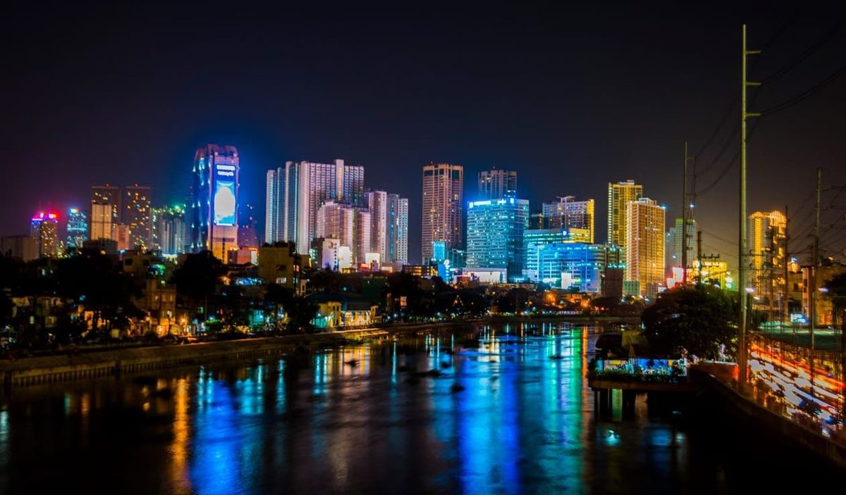 The Manila skyline lit up at night, reflected in the river below
